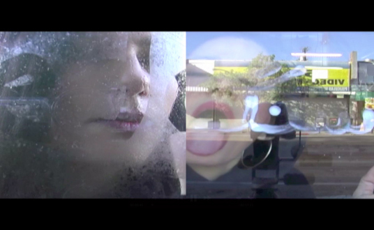 Iran via Video Current – a screening curated by Amirali Ghasemi and Sandra Skurvida - Amitis Motevalli: Love Letters to Jeremy/Let Them Eat Yellowcake, 2011. Video, 12:00 min, image courtesy the artist and OtherIS.

Love Letters to Jeremy/Let Them Eat Yellowcake* is a video derived from a performance, conceived in two parts to be shown simultaneously in Iran and outside Iran (the first simultaneous showing was to be in March 2011 at Aaran gallery, Tehran, and Morono Kiang gallery, Los Angeles, as part of My Superhero exhibition curated by Nazila Noebashari; only the “outside” segment has been shown there). In Part I, I am on the outside of a window looking in. I steam the window with my breath and write words backward onto the glass, English words such as on-the-edge and tee-ter, that indicate a position that does not fit-in or conform to a standard. As each word sequence begins to fade, I wipe it with my hand and blow onto the window to write again. With each word, I become light-headed due to the heavy breathing. In Part II, I perform inside the café looking out. I write backward in Farsi with whipped cream onto the window in order to communicate with the outside. The words that I write play with language and have multiple meanings. After each word is written, I lick the cream off of the window. With this set of words, I maintain a certainty and awareness. Words with specific connotations are used to engage the viewers and place them either inside or outside the window. When writing Farsi, I am inside, you are out. When writing English, I am outside, you are in. Regardless of position, context, and environment, I initiate a dialogue; in Part I, it leaves me breathless, in Part II, it nourishes me.

* Yellowcake is slang for Uranium.